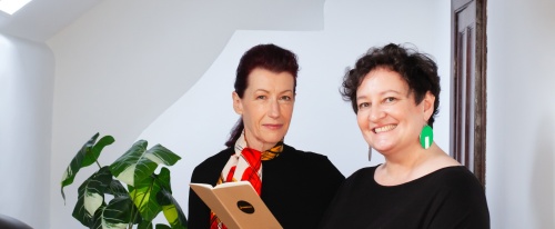 Dominique Antarakis and Jan Chisholm smiling at camera with a noteboook in hand