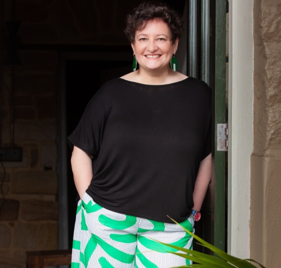 Dominique leaning on doorframe with hands in pockets, smiling at camera