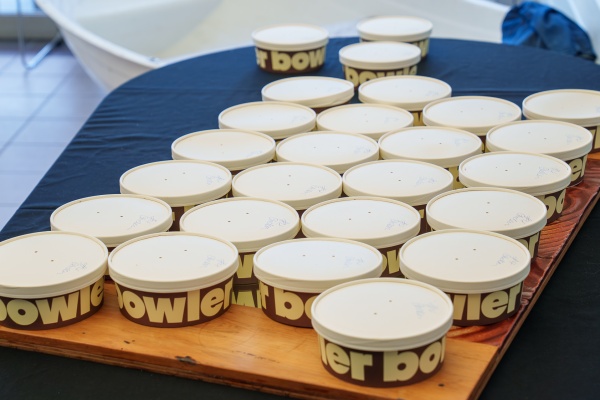 Containers of food sit arrange din rows on a table. They are brown and read 'Bowler' in a pale yellow, lowercase font.