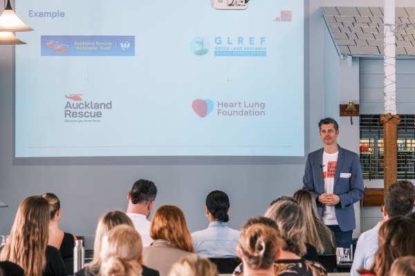 Tim Dove stands before an audience. Behind him is a presentation showing the before and after of companies who have rebranded. The new brand identities are simplified, but carry greater emotional and visual impact.