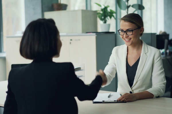 Two women shaking hands across a work desk.